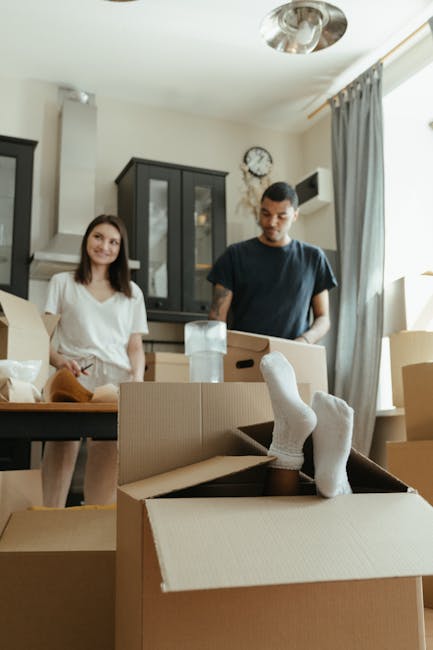 Inside a home during the packing process for a house move, three clearly labeled cardboard boxes are stacked on a wooden floor. The top box has the word 'STUFF' written on it in red marker, accompanie